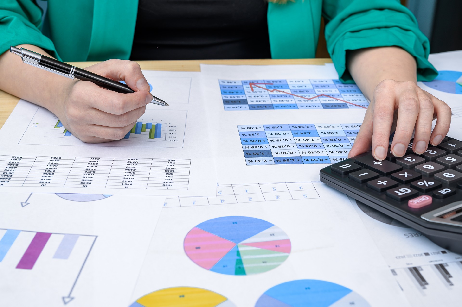 A woman sits at a desk at work, counts on a calculator, and papers with charts and data around her